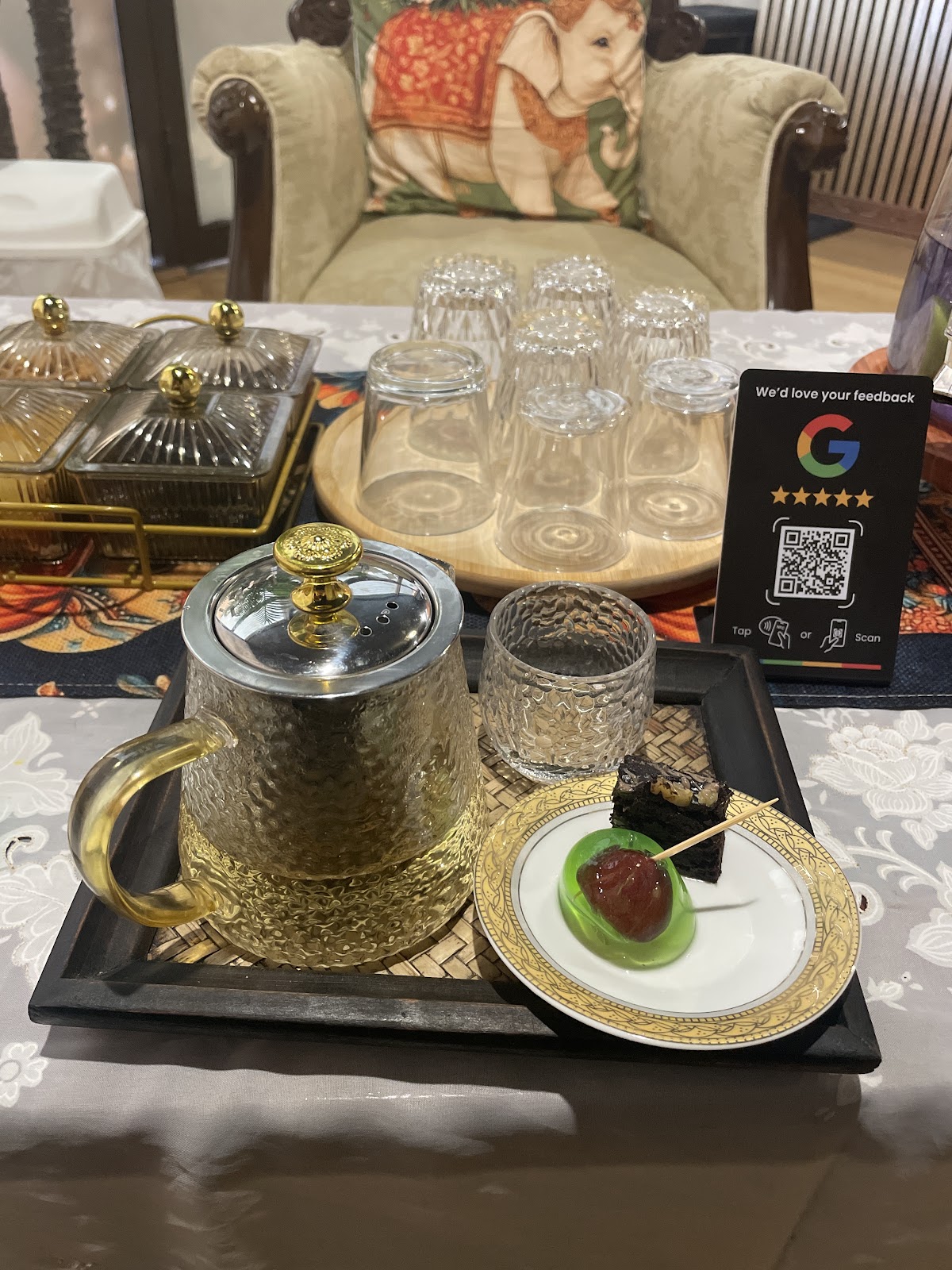 A glass teapot and a slice of cake on a gold tray